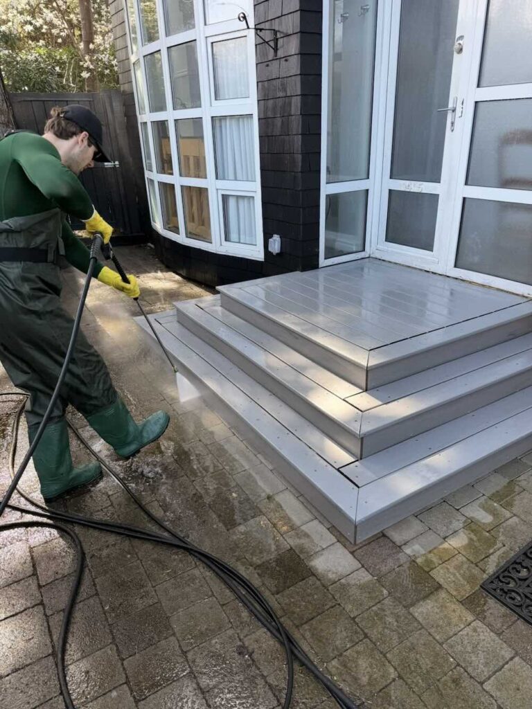 Pacific Breeze Services technician pressure washing a paver patio beside composite front steps in South Surrey